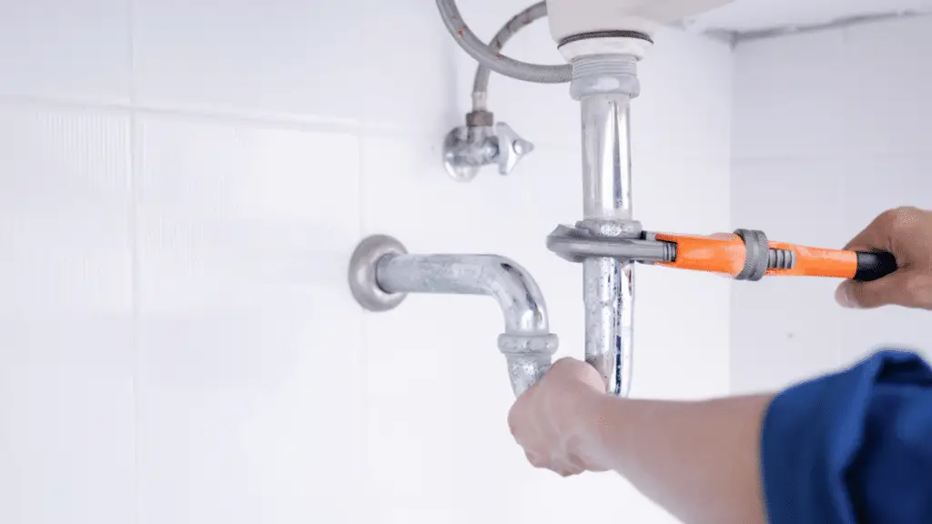 A close up of the pipes under a sink being adjusted with a wrench.