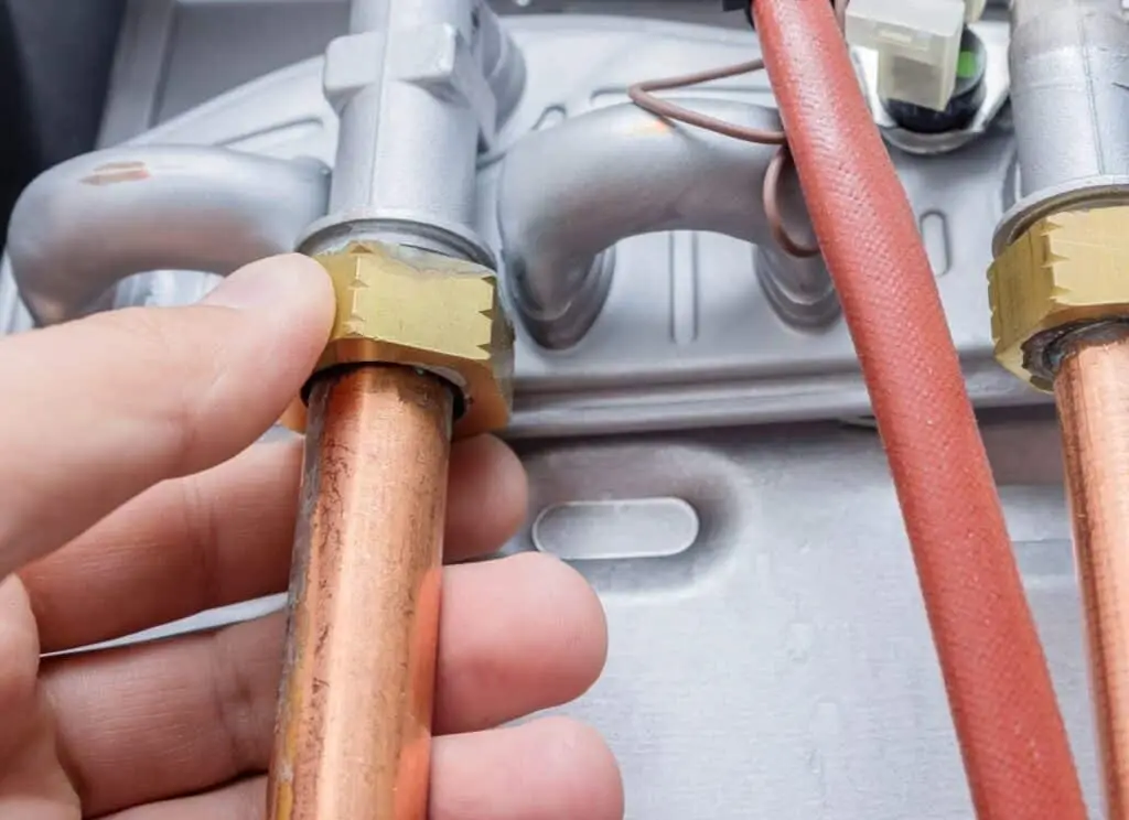 A person is holding a copper pipe next to a water heater, demonstrating plumbing work or installation.