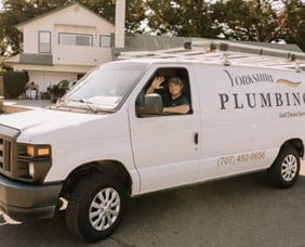 A man seated in the driver's seat of a van, focused on the road ahead, with a calm expression on his face.