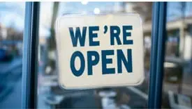 A bright "We're Open" sign displayed prominently in a shop window, inviting customers to enter and explore.